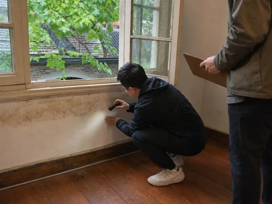 A renter inspecting an older Shanghai apartment for rainwater leaks around a wooden window